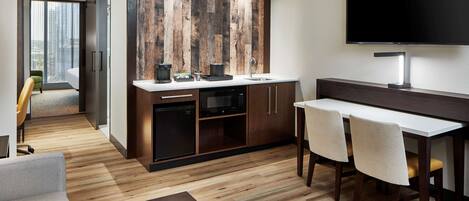 A modern kitchen with a wooden accent wall, a flat-screen TV, and a dining area with chairs.