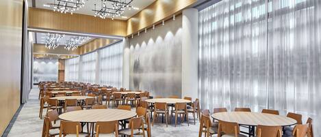 Una amplia sala de conferencias con varias mesas redondas y sillas, ventanas grandes con cortinas translúcidas e iluminación moderna.