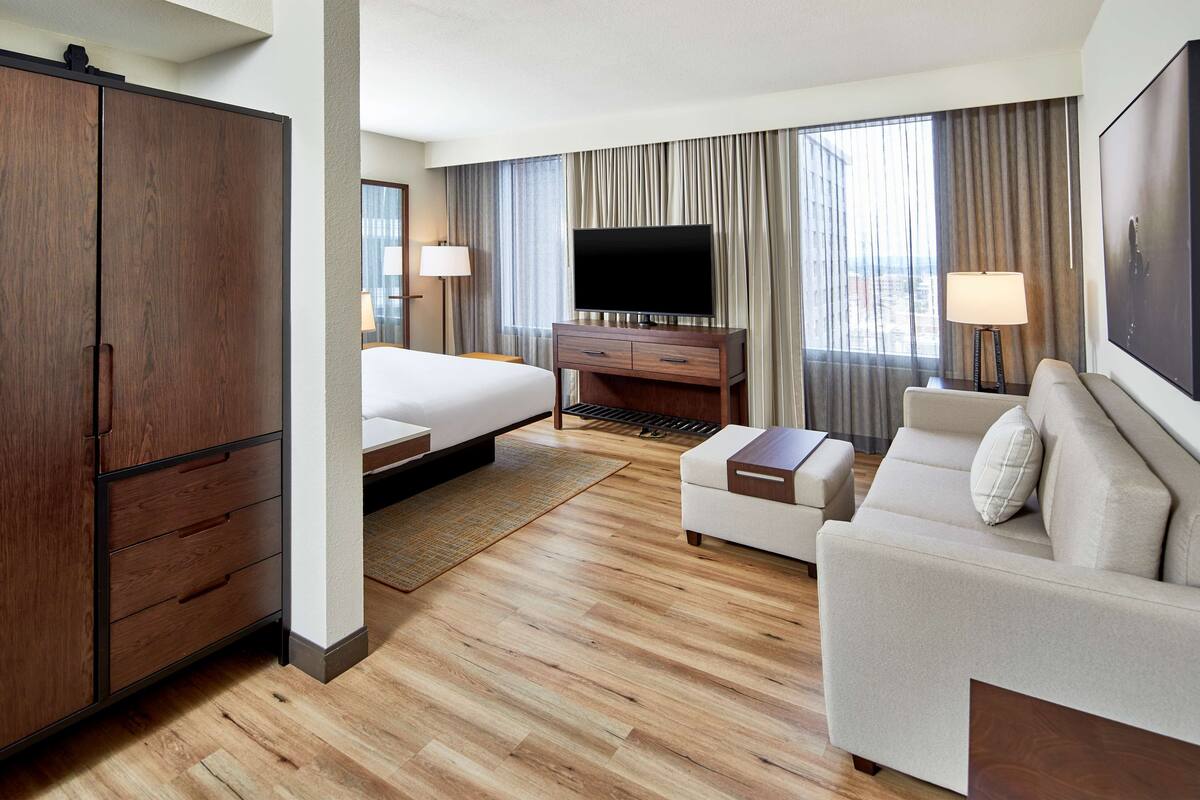 A hotel room with a large bed, a sofa, a TV, a desk, and a wardrobe.