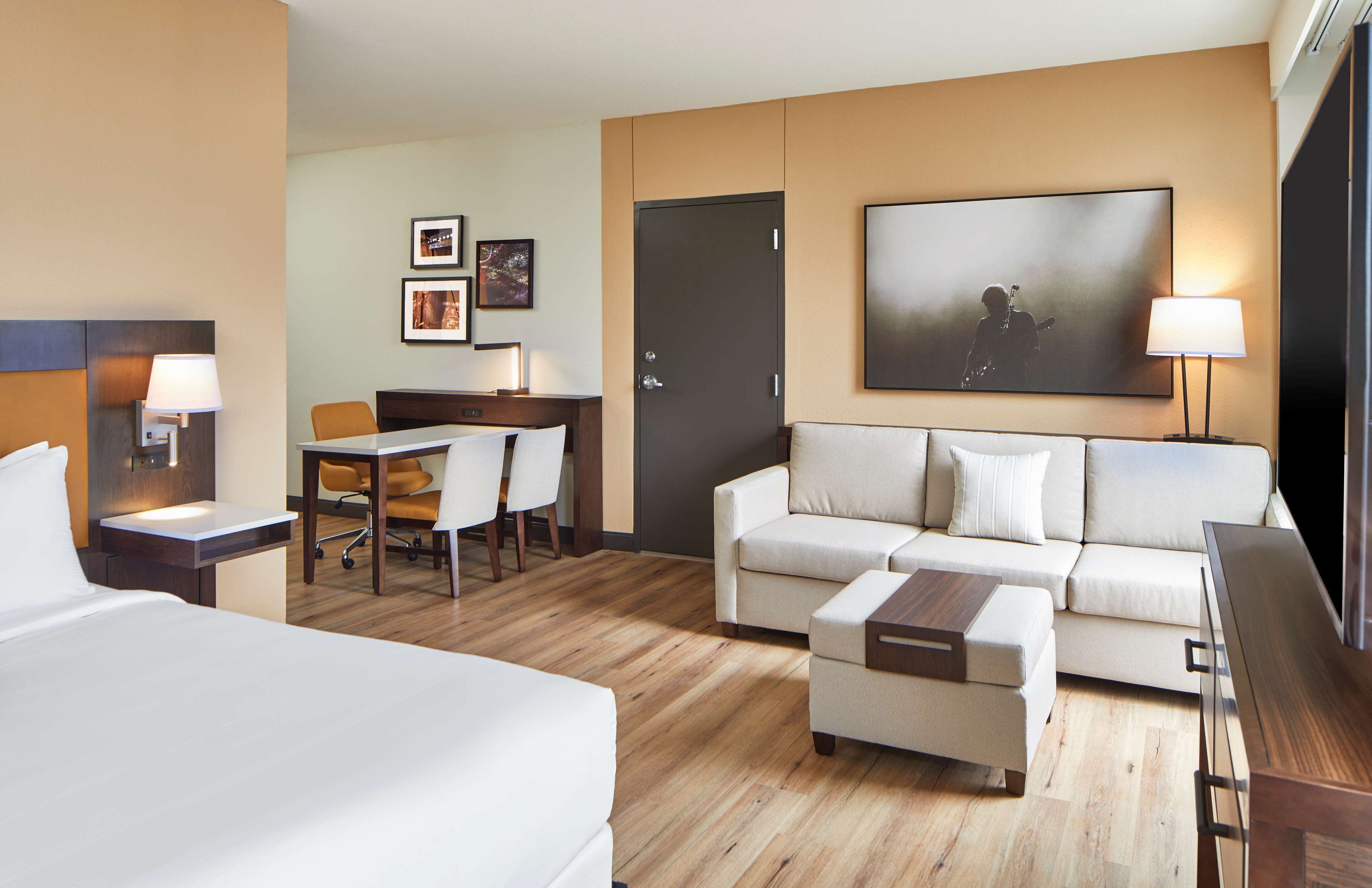 Une chambre d’hôtel avec un lit, un canapé, un bureau avec une chaise, une télévision et une porte.