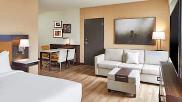 Quarto de hotel com cama, sofá, escrivaninha com cadeira, televisão e porta.