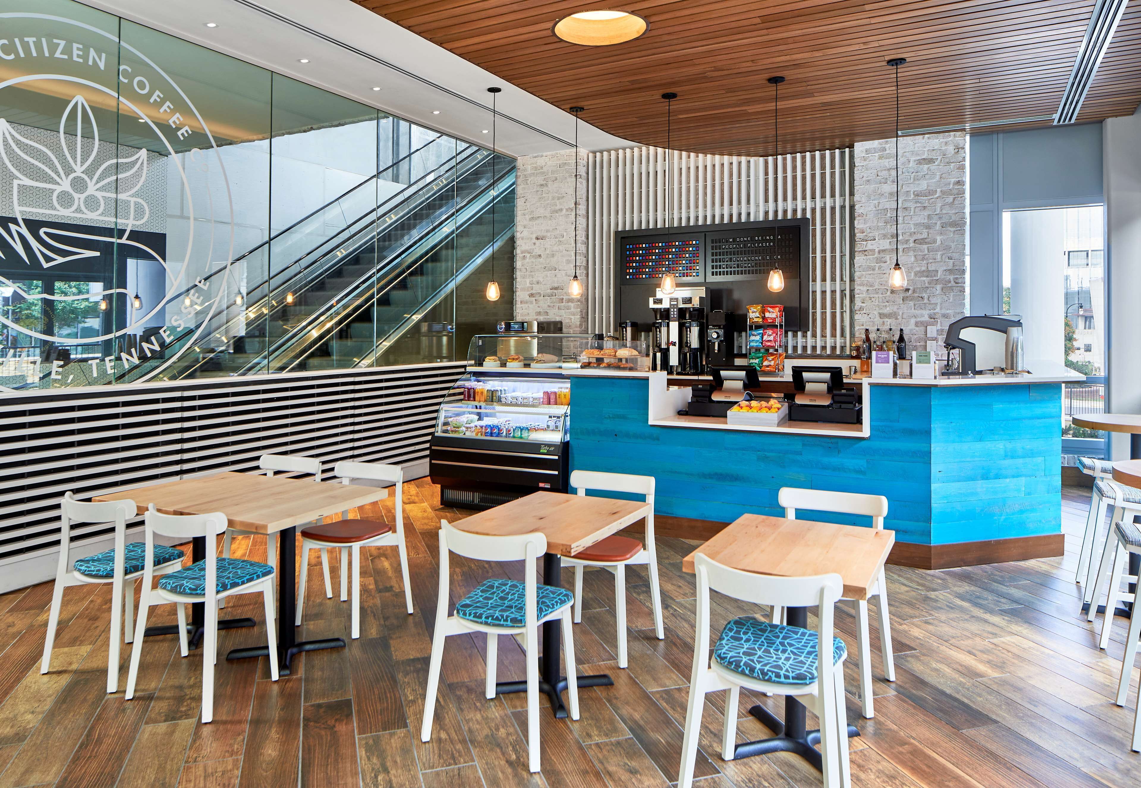 A modern coffee shop interior with a central counter, seating area, and a visible staircase.