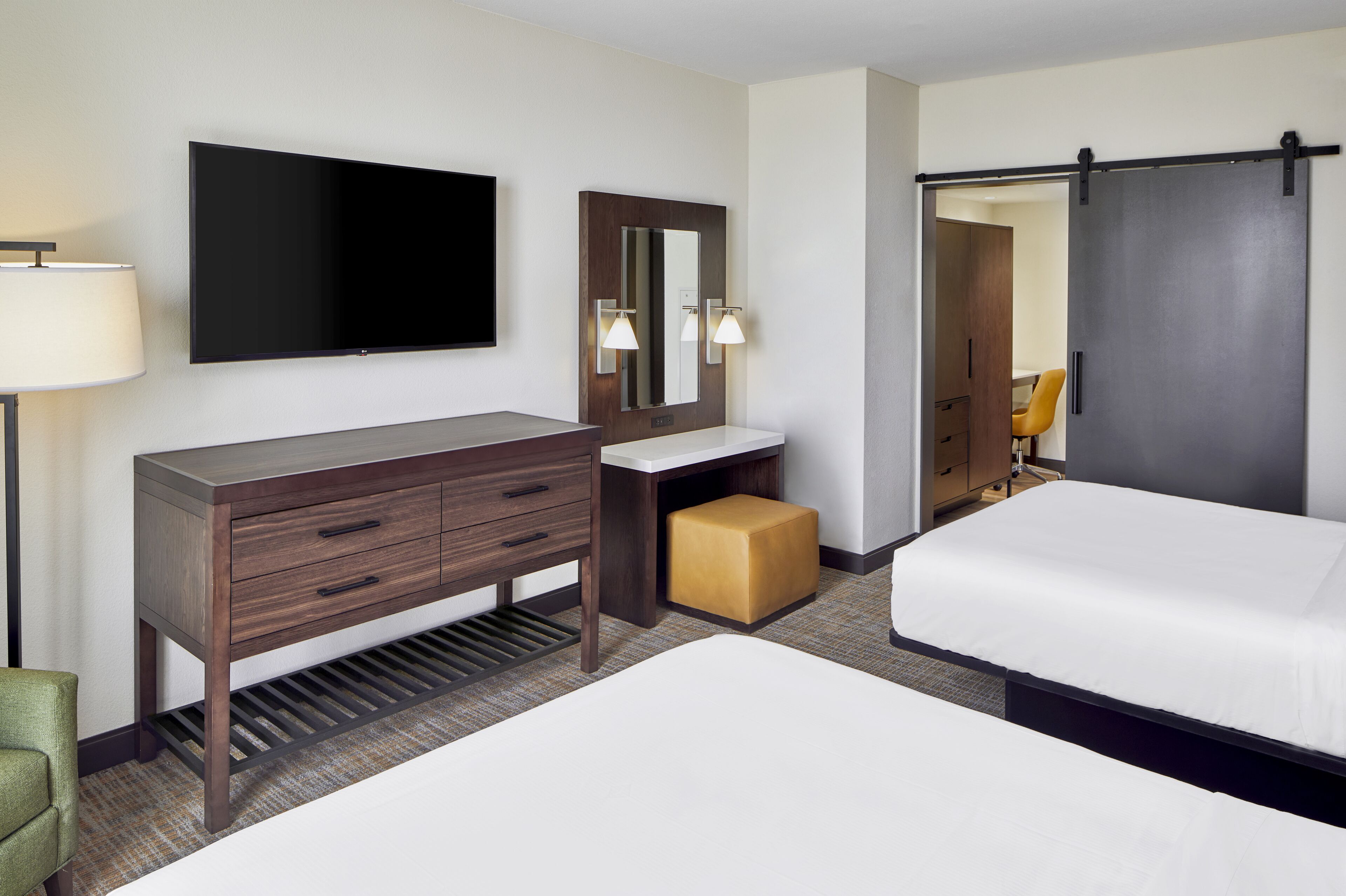 A hotel room with a bed, a desk with drawers, a flat-screen TV, a mirror, and a sliding door closet.