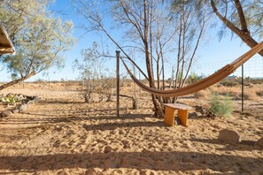 Relax in a serene outdoor setting with a hammock and nearby bench amidst a natural landscape.