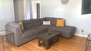 A gray sectional sofa with two yellow pillows, a small wooden coffee table, and a glass side table.