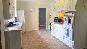 A kitchen with white cabinets, a refrigerator, a microwave, and a stove. There is a door leading to another room.