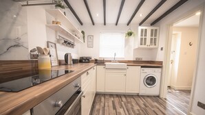 Une cuisine moderne avec des plans de travail en bois, un four encastré, un lave-linge et une fenêtre équipée de stores.