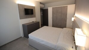 A modern bedroom with a bed, a dresser, a TV mounted on the wall, and a wardrobe.