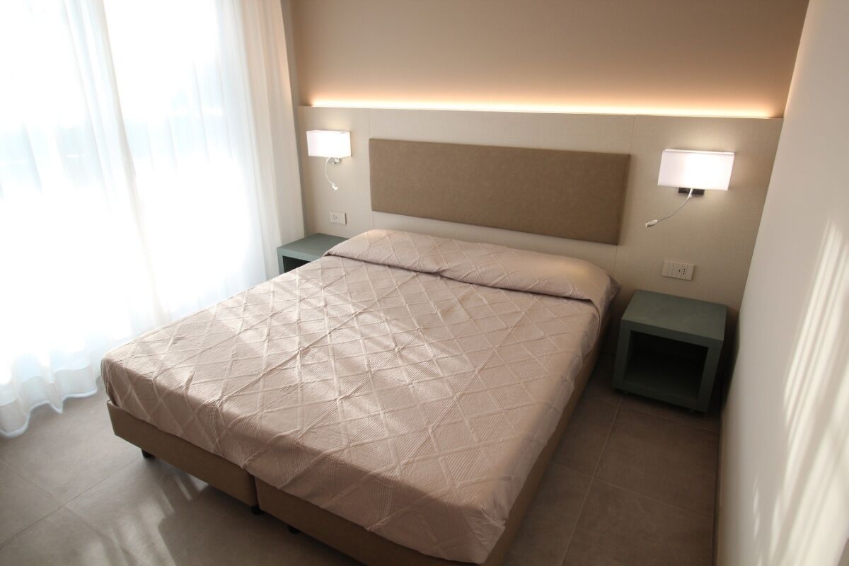 Une chambre d’hôtel avec un grand lit, deux tables de chevet et une tête de lit dotée d’un éclairage intégré.