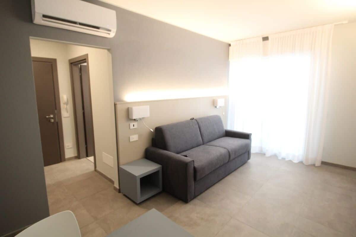 Un salon moderne avec un canapé gris, une petite table d’appoint et une lampe fixée au mur.