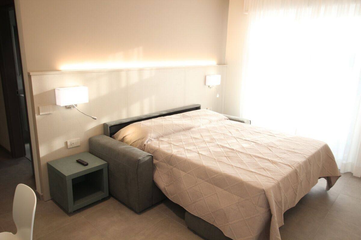Une chambre d’hôtel bien rangée, avec un lit, des tables de chevet, une chaise et une lampe.