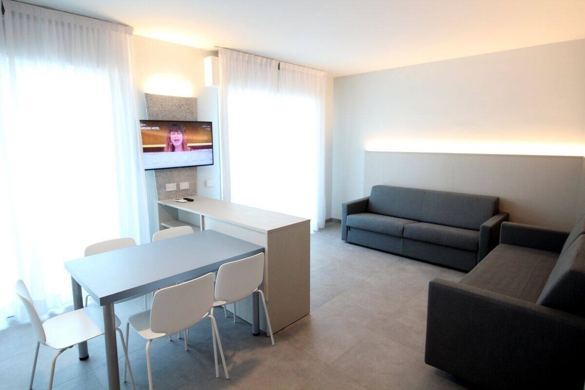 Une chambre d’hôtel moderne avec un coin repas, un canapé et un téléviseur fixé au mur.