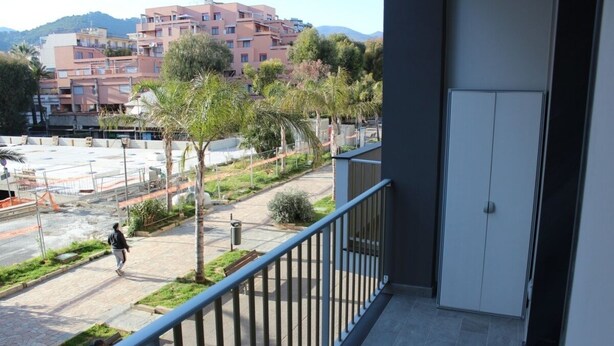A balcony with a view of a residential area, including a road and buildings in the background.