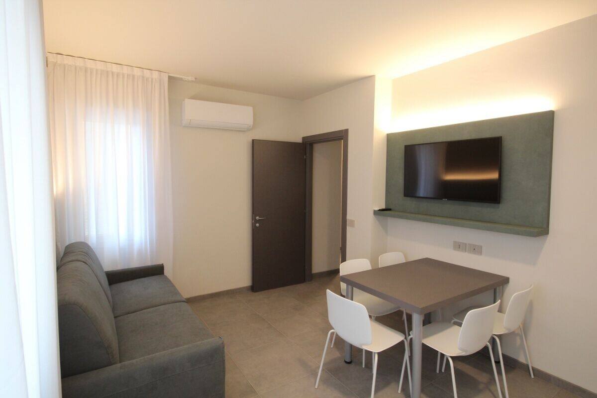 Un salon moderne comprenant un canapé, une table à manger avec des chaises, un téléviseur à écran plat fixé au mur et une porte.