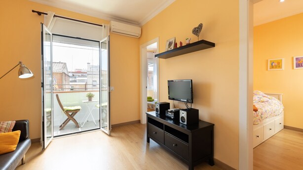 A modern bedroom with a sliding glass door leading to a balcony, a black TV stand, and a bed with a floral bedspread. - Casa Flors - 2 bedroom apartment with free wifi (Barcelona)