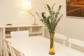Una mesa blanca con un florero de vidrio que contiene follaje verde.