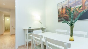A modern dining area with white furniture, a painting of a cityscape, and a plant in a vase. - Apartment SF C - 3 bedrooms 5 pax - 300 meters from Sagrada Familia - FREE WIFI (Barcelona)