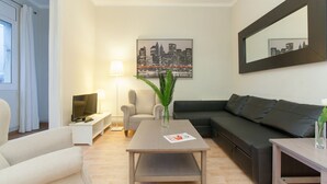 A modern living room with a sofa, a coffee table, a lamp, and a cityscape painting. - Apartment SF C - 3 bedrooms 5 pax - 300 meters from Sagrada Familia - FREE WIFI (Barcelona)