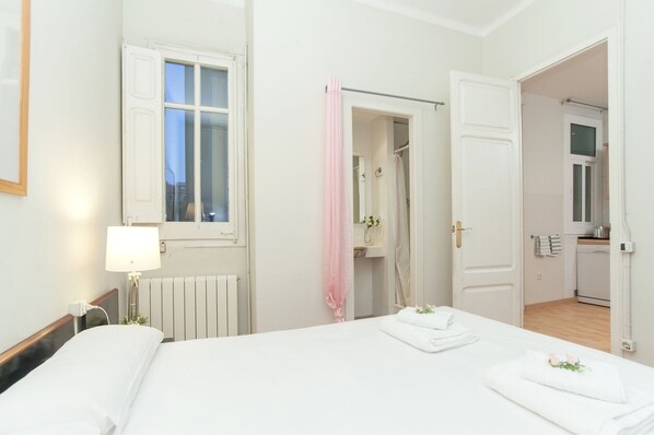 Habitación de hotel con cama, ventana, baño con ducha y kitchenette.