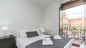 A hotel room with a bed, bedside tables, a nightstand, a window with a view of a building, and a balcony with chairs and potted plants. - Gaudí Views- Suite with view on Hospital Sant Pau (UNESCO Heritage)  - FREE WIFI (Barcelona)