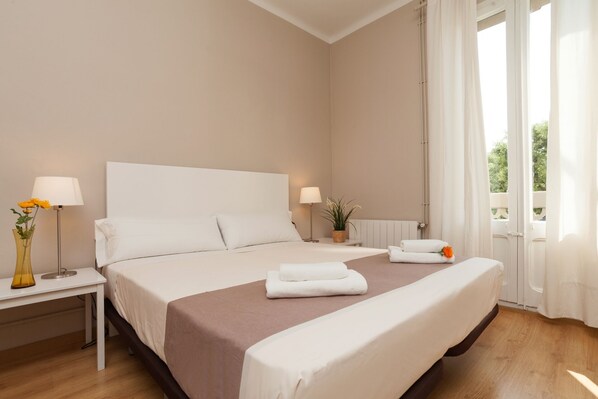 A hotel room with a large bed, bedside tables, a lamp, and a view of greenery outside.