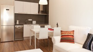 Une cuisine moderne avec des armoires blanches, un réfrigérateur en acier inoxydable et un lave-vaisselle. On y trouve également un coin repas avec une table et des chaises blanches.