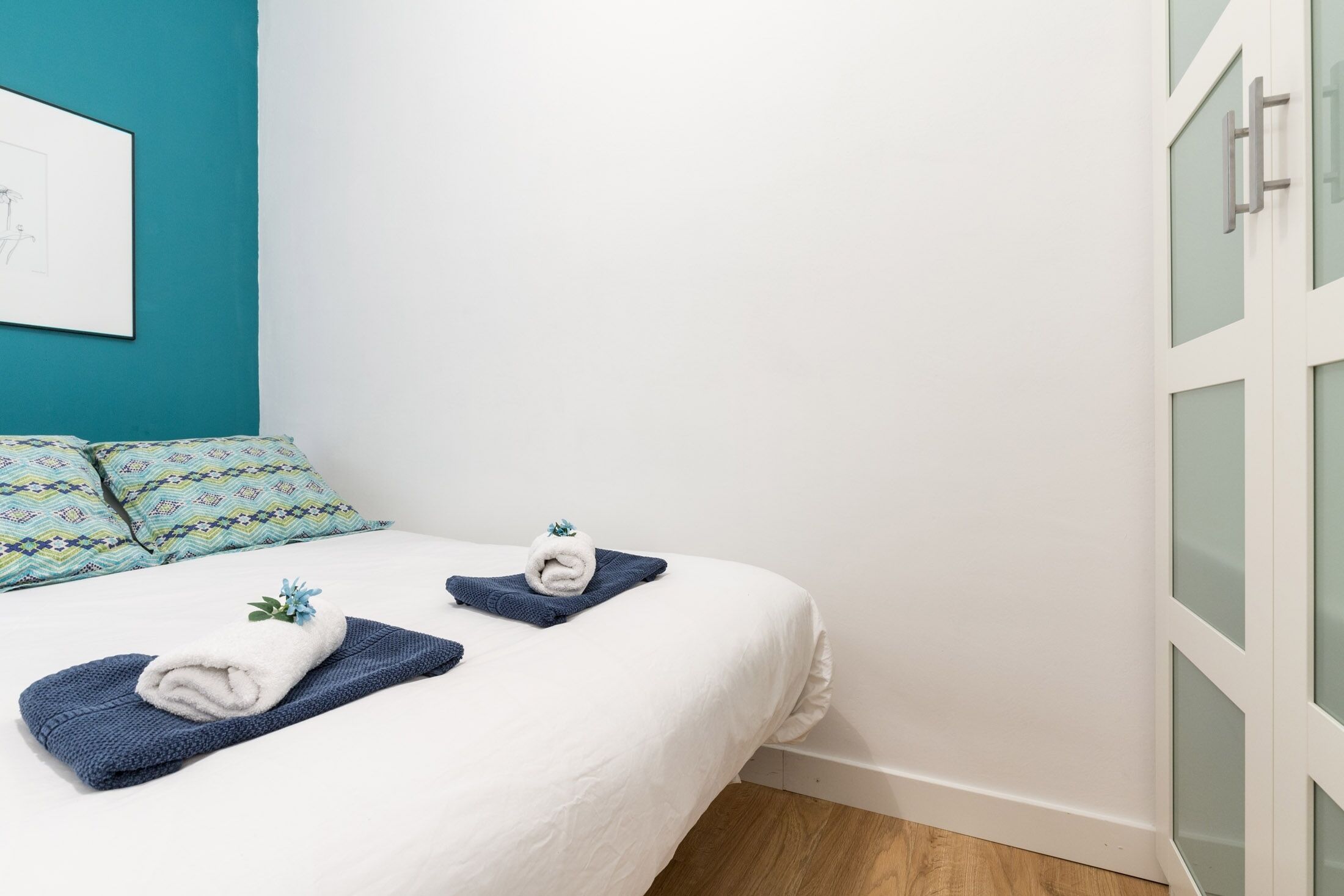 A neatly made bed with white and blue linens, a blue towel, and a decorative item on the bed.