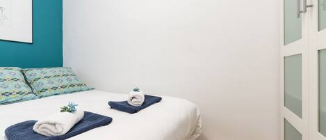 A neatly made bed with white and blue linens, a blue towel, and a decorative item on the bed.