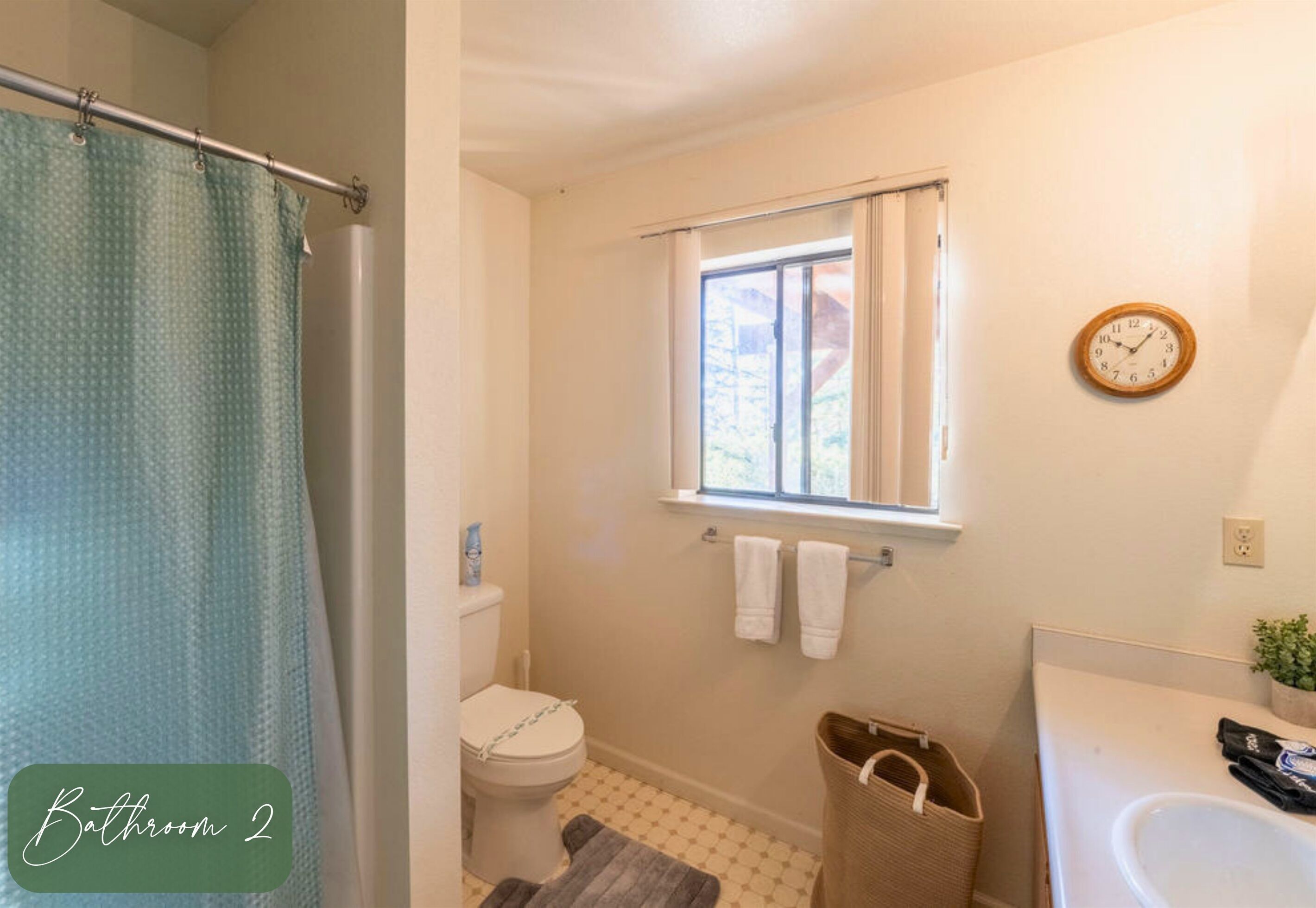 A bathroom with a toilet, a window, a clock, and a towel rack.