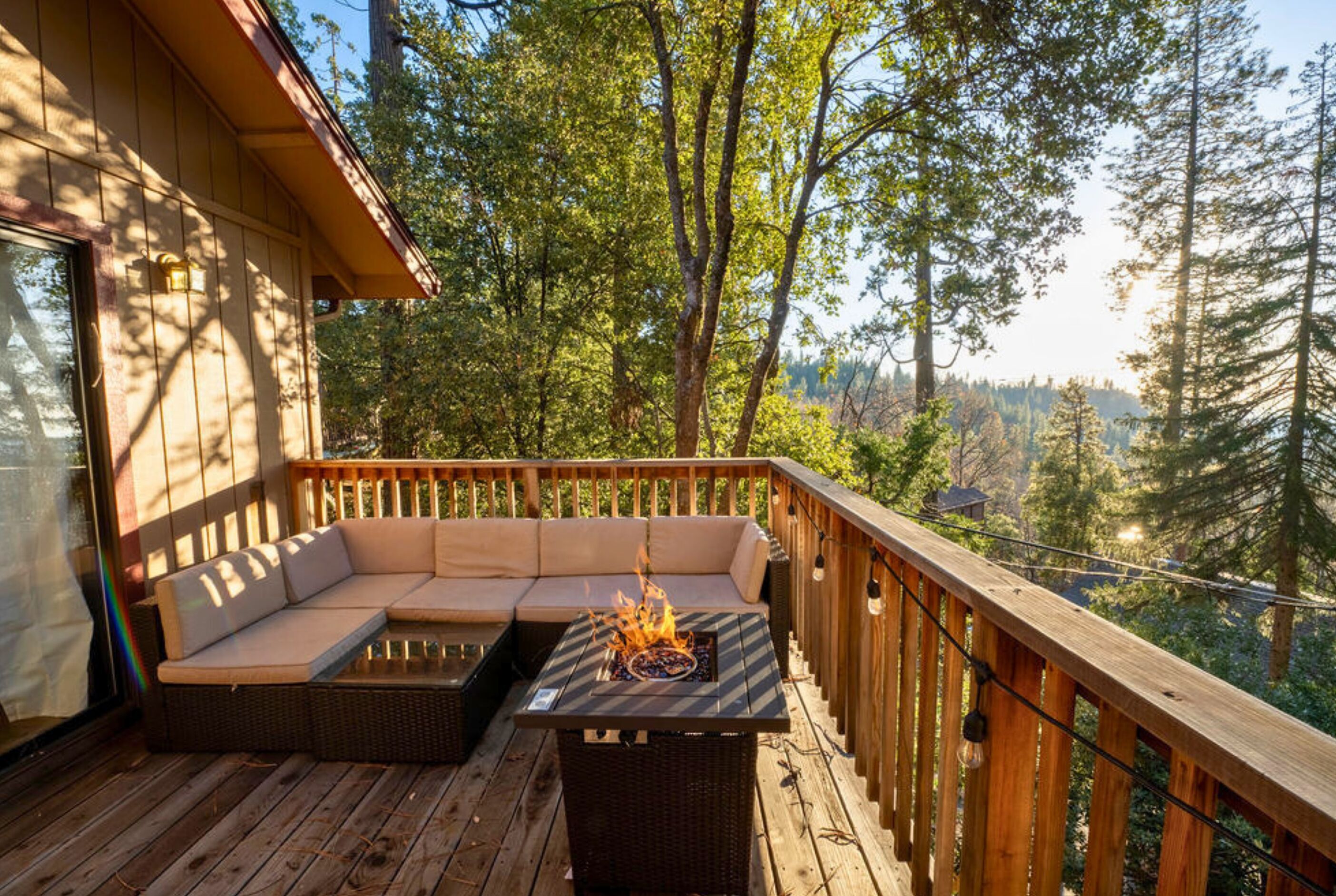 A wooden deck with a sofa and a fire pit, surrounded by trees.