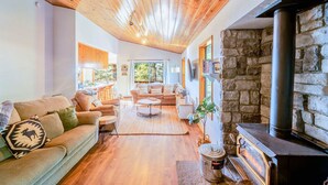 A cozy living room with a stone fireplace, wooden ceiling, and a comfortable seating area. - Serenity in the Pines: Cozy Mountain Retreat (Twain Harte)