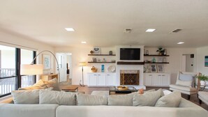 A modern living room with a sofa, coffee table, and a fireplace. There is a television mounted on the wall and a window providing natural light. -  Beautiful Lake Front Home All Decked Out and Ready for Fun (Malakoff)