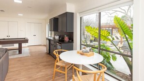A modern kitchen with dark cabinets, a dining area with a round table and chairs, and a large window with a view of outdoor seating. -  Beautiful Lake Front Home All Decked Out and Ready for Fun (Malakoff)
