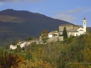 A historic building with a prominent tower, situated on a hillside with surrounding vegetation.