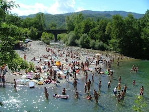 A crowded riverside area with people swimming and sunbathing.