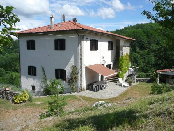 A two-story house with a red-tiled roof, a patio with outdoor furniture, and a staircase leading to the upper floor.