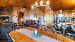 A spacious living area with a wooden ceiling, a fireplace, a dining table with chairs, and a kitchen with wooden cabinets and appliances. - Blue Ridge Blessing - Pet Friendly! Views, hot tub, great location on App Ski Mtn! (Blowing Rock)