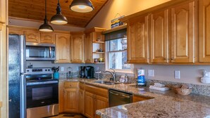 A kitchen with wooden cabinets, granite countertops, stainless steel appliances, and pendant lighting. - Blue Ridge Blessing - Pet Friendly! Views, hot tub, great location on App Ski Mtn! (Blowing Rock)