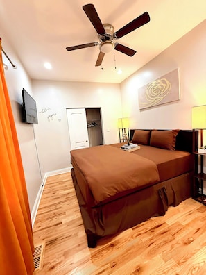 Une chambre à coucher avec un lit, un ventilateur de plafond, une télévision, une armoire et un tableau au mur.