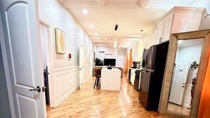 A spacious living area with wooden flooring, white walls, and a kitchen in the background. - Modern Chicago Getaway • Sleeps 6 • Near Downtown (Chicago)