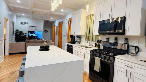 A modern kitchen with white cabinets, a central island, a stove, and a microwave. - Modern Chicago Getaway • Sleeps 6 • Near Downtown (Chicago)