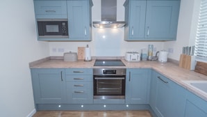 A compact kitchen with blue cabinets, a microwave, a stove, and a toaster. - Seashells Cottage (Lytham St. Anne's)