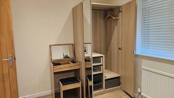 A room with a wooden wardrobe, a mirror, a bench, and a window with blinds.