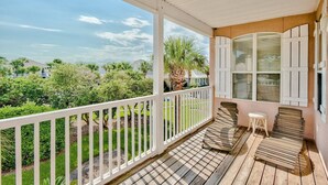 A covered porch with a view of a residential area, a wooden bench, and a small stool. - 23 Aquamarine • Private Beach Access • Golf Cart • 2 Pools • Beach Gear • Tennis (Destin)