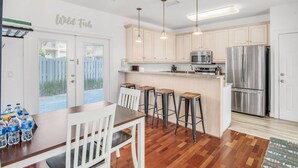 A modern kitchen with white cabinets, stainless steel appliances, and a wooden dining table with bar stools. - 23 Aquamarine • Private Beach Access • Golf Cart • 2 Pools • Beach Gear • Tennis (Destin)