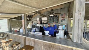 A rustic bar with wooden stools and a counter, featuring a menu board and an American flag. - 23 Aquamarine • Private Beach Access • Golf Cart • 2 Pools • Beach Gear • Tennis (Destin)
