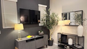 A modern living room with a flat-screen TV, a console table, a potted plant, and a mirror. - Desert Olive Retreat - Sleeps 4- 5 min fr Verrado Marketplace 30 min fr airport (Buckeye)