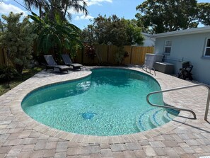 A rectangular swimming pool with a tiled edge, surrounded by a brick patio.