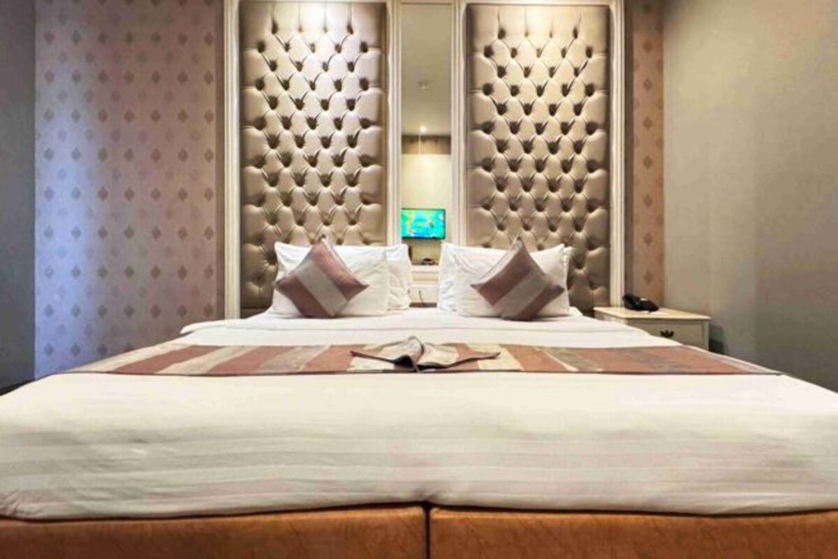 A large bed with a tufted headboard, two bedside tables, and a mirror.