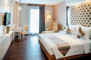 A hotel room with a large bed, a desk, a chair, a television, and a window with curtains. - Savero Hotel (Depok)